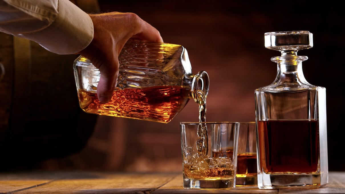 Person's Hand Pouring Whisky from Bottle into a Glass